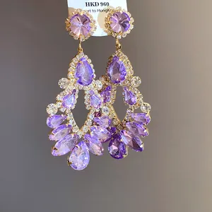 Close-up of ornate palace style earrings with purple teardrop crystals and gold setting