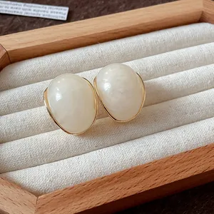 Elegantes pendientes de resina marbreada crema con borde dorado en expositor de joyas.