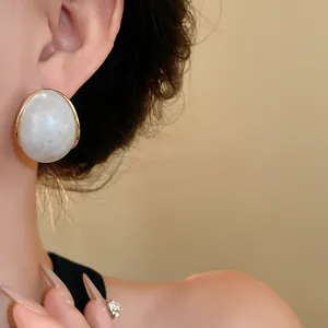 Detalle de pendiente de resina jaspeada retro usado en la oreja con borde dorado