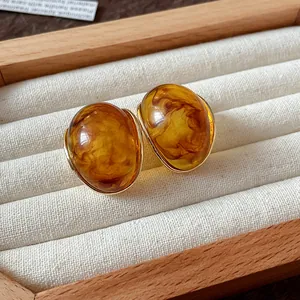 Detalle de pendientes vintage de resina con textura de ámbar y borde de oro fino