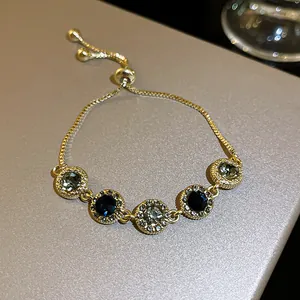 Close-up of elegant gold drawstring bracelet with dark blue and emerald green zircon stones.