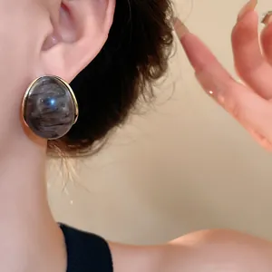 Detalle de pendientes de resina con patrón de mármol retro y borde dorado en una modelo