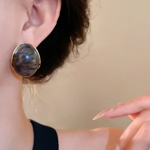 Vista detallada de un elegante pendiente de resina con efecto mármol en una modelo.