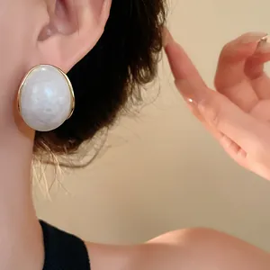 Vista de detalle de pendientes geométricos de resina veteada blanca y marco dorado