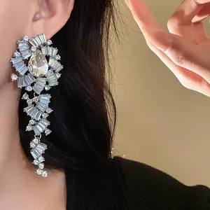 Detailweergave van grote zilveren druppeloorbellen versierd met fonkelende strass-steentjes.