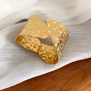 Detalle de un brazalete dorado con textura irregular sobre fondo de tela blanca