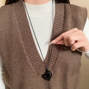 Nahaufnahme einer schwarzen Herz-Halskette, getragen über einer braunen Strickweste.