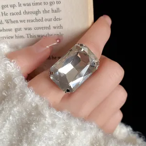Vista dettagliata di un anello con grande gemma rettangolare al dito con uno sfondo libro.