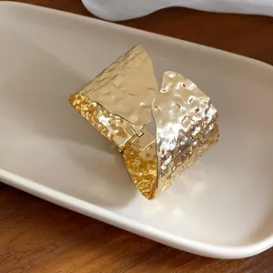 Primer plano de un brazalete dorado martillado minimalista e irregular en una bandeja blanca