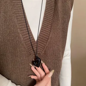 Detailansicht einer unregelmäßigen schwarzen Herz-Halskette getragen zu einem braunen Pullover