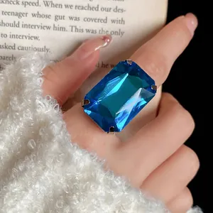 Primo piano di un anello con una grande gemma blu rettangolare sulla mano di una modella.