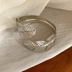 Primer plano de un elegante brazalete abierto con forma de pluma plateada y textura plisada
