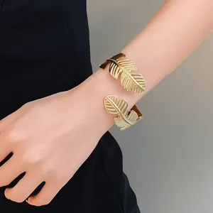 Elegante primer plano de un brazalete abierto con forma de hoja dorada en la muñeca de mujer