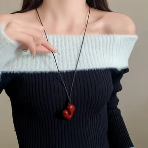 Detailaufnahme eines roten unregelmäßigen Herzanhängers an einer schwarzen Kordelkette