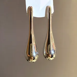 Minimalist high-shine gold water drop pendant earrings featuring silver needle studs