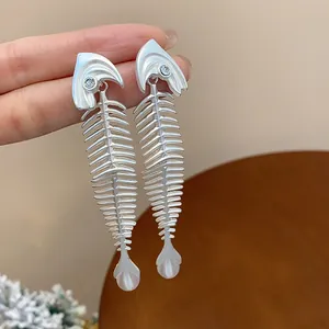 Close-up of unique silver fish skeleton earrings with zircon eyes and pearl drops