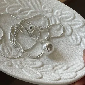 Detail showing the textured silver ball pendant on an elegant snake chain necklace