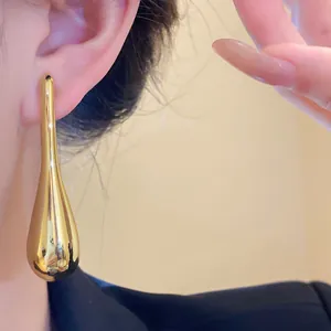Close-up of minimalist gold teardrop pendant earrings showing high-shine metallic finish