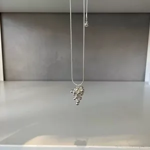 Close-up detail of a minimalist silver necklace with a grape-cluster spherical pendant.