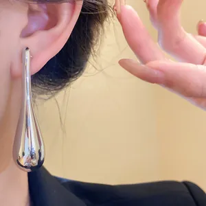 Macro detail view of a minimalist glossy silver teardrop earring worn on a model ear