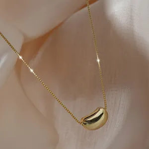 Minimalist gold stainless steel acacia bean necklace displayed on elegant draped fabric