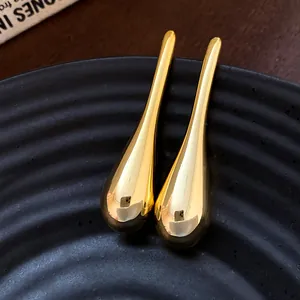 Detailed close-up of polished gold-tone teardrop earrings on black textured plate