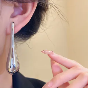 Close-up detail of oversized silver teardrop earring on model with warm indoor lighting