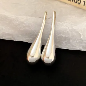 Detailed macro view of minimalist silver teardrop pendant earrings on textured paper