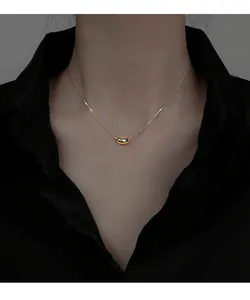 Detailed close-up showing a minimalist gold bean pendant necklace on a female model