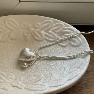 Macro view of a brushed silver heart pendant necklace lying on a textured white plate.