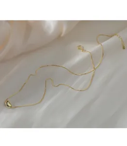 Macro view of a elegant gold bean pendant necklace resting on white silk fabric