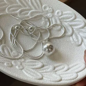 Detailed close-up view of a brushed silver sphere pendant on a fine snake chain necklace