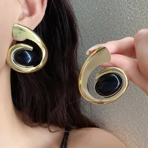 Detail van grote gouden geometrische spiraal oorbellen met zwarte ovale steeninleg