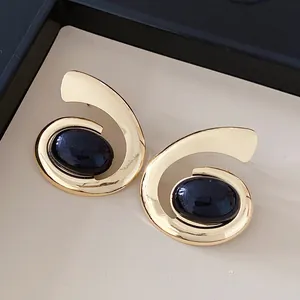 Detailweergave van geometrische gouden spiraal oorbellen met donkerblauwe ovale stenen.