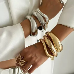 Primer plano de brazaletes metálicos ondulados apilados en oro y plata en modelo