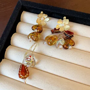 Close-up of asymmetric vintage earrings with amber beads and gold flower studs in a display box.