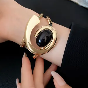 Detailweergave van een geometrische gouden spiraalarmband met een zwarte steen.