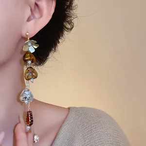 Detailed view of long asymmetrical flower tassel earrings on an Asian model's ear.