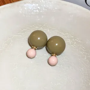 Detail von bonbonfarbenen Doppelperlen-Ohrringen mit Edelstahlstiften auf Keramikteller.