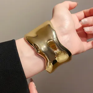 Primer plano de un brazalete de metal dorado irregular grueso usado en una muñeca.