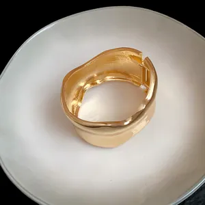 Detalle de cerca de un brazalete de metal dorado irregular ondulado sobre plato blanco