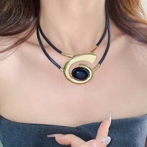 Detail van geometrische gouden spiraalketting met een grote donkere cabochon steen