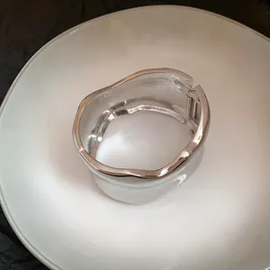 Vista detallada de un brazalete ancho de metal plateado irregular con cierre de bisagra