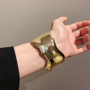 Detalle del brazalete de metal dorado pulido con diseño ondulado irregular