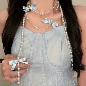 Dettaglio di una collana di perle a più strati con delicati fiocchi di nastro celeste.