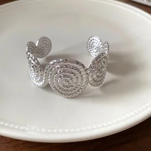 Silver textured spiral cuff bracelet with artistic pleated design on white plate