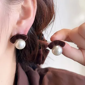 Macro view of elegant dark brown flocked velvet bow and pearl stud earrings being worn.