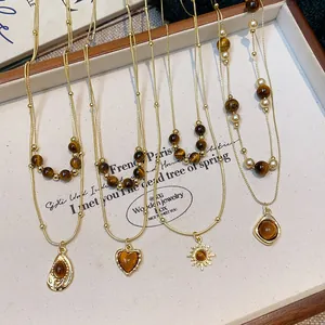 Detailed shot of gold-layered necklaces featuring tiger's eye beads and unique pendants.