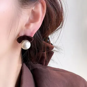 Close-up of elegant flocked bow pearl ear studs on an ear, showcasing velvet texture.