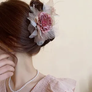 Primo piano elegante di un fermaglio per capelli con fiore rosa antico e piume su uno chignon
